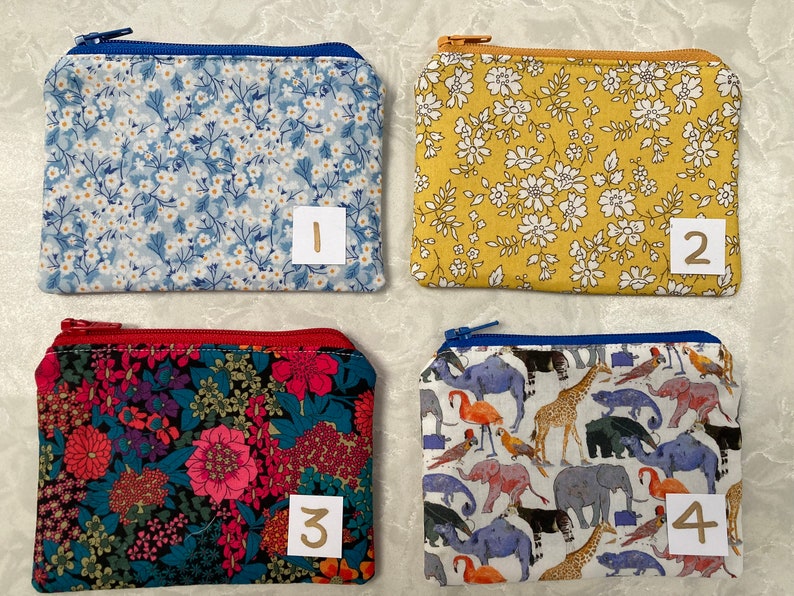 Op de afbeelding: Vier kleine etuis met ritssluiting met verschillende bloemen- en dierenpatronen. De etuis zijn rechthoekig en hebben een ritssluiting. De eerste is lichtblauw met witte bloemen. De tweede is geel met witte bloemen. De derde is rood met bloemen. De vierde is wit met dieren.