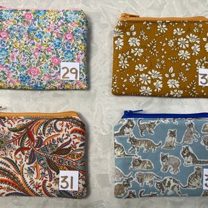 Op de afbeelding: Vier kleine etuis met ritssluiting met verschillende stofpatronen. E&eacute;n heeft een bloemenpatroon met roze, blauwe en gele bloemen. Een andere is mosterdkleurig met witte bloemen. De derde heeft een paisley-ontwerp en de vierde een kattenpatroon.