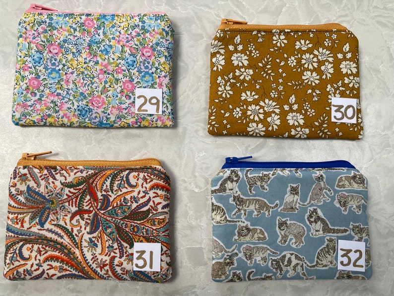 Op de afbeelding: Vier kleine etuis met ritssluiting met verschillende stofpatronen. E&eacute;n heeft een bloemenpatroon met roze, blauwe en gele bloemen. Een andere is mosterdkleurig met witte bloemen. De derde heeft een paisley-ontwerp en de vierde een kattenpatroon.