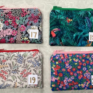 Op de afbeelding: Vier kleine, rechthoekige etuis met ritssluiting met bloemen- en tropische patronen. De etuis hebben verschillend gekleurde ritsen en zijn genummerd met de nummers 17, 18, 19 en 20 op kleine witte labels. De etuis zijn waarschijnlijk bedoeld voor het dragen van kleine voorwerpen.