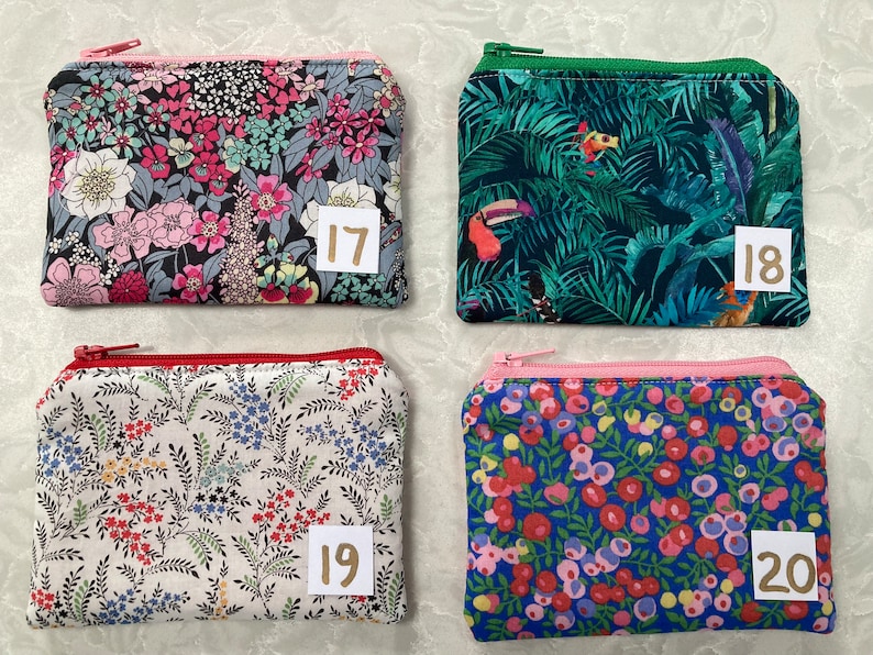Op de afbeelding: Vier kleine, rechthoekige etuis met ritssluiting met bloemen- en tropische patronen. De etuis hebben verschillend gekleurde ritsen en zijn genummerd met de nummers 17, 18, 19 en 20 op kleine witte labels. De etuis zijn waarschijnlijk bedoeld voor het dragen van kleine voorwerpen.