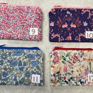Op de afbeelding: Vier kleine, rechthoekige etuis met ritssluiting en bloempatronen. De etuis hebben verschillende gekleurde ritsen en stofpatronen, waaronder roze bloemen, konijnen, blauwe bloemen en gemengde bloemen. Elke etui heeft een nummer op een klein wit label.