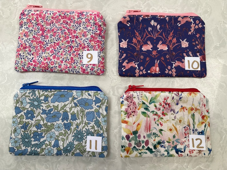 Op de afbeelding: Vier kleine, rechthoekige etuis met ritssluiting en bloempatronen. De etuis hebben verschillende gekleurde ritsen en stofpatronen, waaronder roze bloemen, konijnen, blauwe bloemen en gemengde bloemen. Elke etui heeft een nummer op een klein wit label.