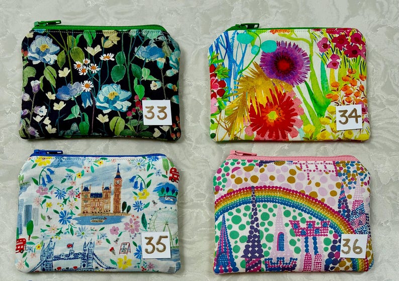 Op de afbeelding: Vier kleine, rechthoekige etuis met ritssluiting met bloemen- en reisthema's. De etuis hebben verschillende gekleurde ritsen en bevatten de nummers 33, 34, 35 en 36 op kleine witte labels.
