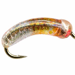 May include: A curved fishing fly lure featuring a translucent, segmented body with internal gold and orange glitter particles. The head is a metallic copper color with a small red accent, and a sharp gold-toned metal hook is attached at the base.