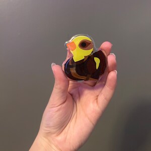 May include: A yellow and brown bird figurine encased in clear resin. The bird is sitting on a branch with its wings spread out.