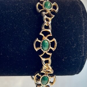 May include: A gold chain bracelet with green oval-shaped stones set in ornate gold cross-shaped settings.