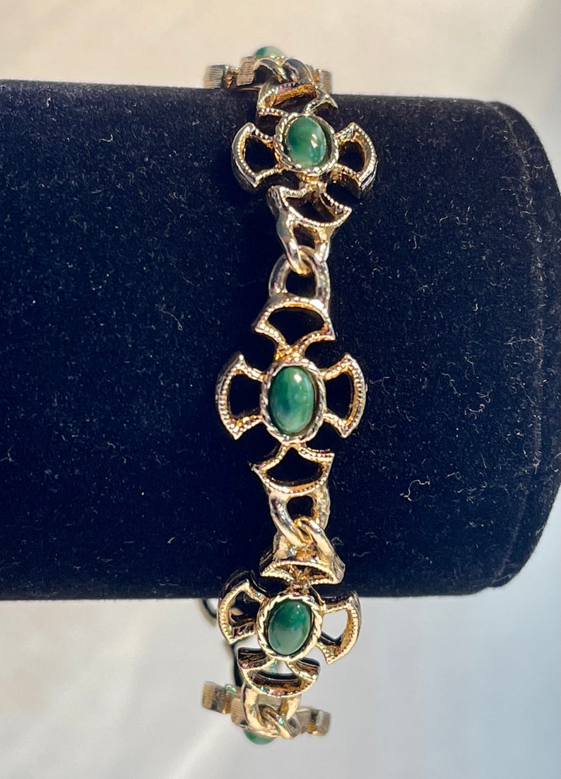 May include: A gold chain bracelet with green oval-shaped stones set in ornate gold cross-shaped settings.