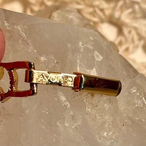 May include: A gold-toned metal bracelet with a clasp that reads "AVON" in all caps.