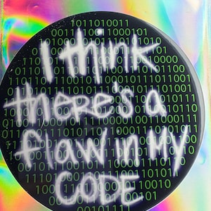 May include: A black and green sticker with white text that reads "I think there's a flaw in my code" surrounded by a pattern of binary code.