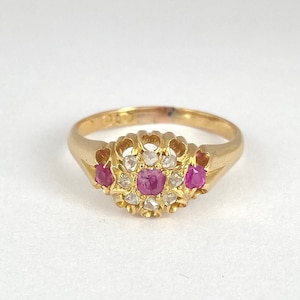 Puede incluir: Un anillo de oro con un grupo de pequeños diamantes y tres rubíes rosas.