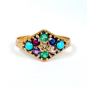 Op de afbeelding: Een gouden ring met een ruitvormige cluster van veelkleurige edelstenen, waaronder twee turkoois cabochons, twee groene stenen, een dieprode steen, een blauwe steen, een paarse steen en een centrale heldere steen in een getextureerde gouden band.