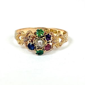 Puede incluir: Un anillo de oro con un grupo de piedras preciosas de colores. El anillo presenta piedras de esmeralda, zafiro, rubí y amatista alrededor de un diamante central. La banda tiene un diseño de filigrana ornamentado.