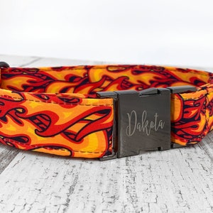 May include: A black and orange dog collar with a metal buckle engraved with the name "Dakota". The collar features a flame pattern.