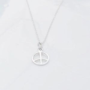May include: A silver peace sign pendant necklace on a white background. Handcrafted Sterling Silver.