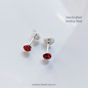 May include: A pair of sterling silver stud earrings with red gemstone accents. Handcrafted sterling silver.