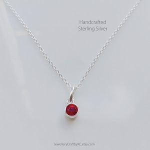 May include: A delicate silver chain necklace with a small, round red gemstone pendant. Handcrafted Sterling Silver.