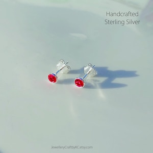 Può includere: Un paio di orecchini a perno in argento sterling realizzati a mano con piccole pietre rotonde di colore rosso brillante.