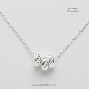 Puede incluir: Un collar de plata con cuatro pequeñas cuentas redondas texturizadas. El collar está hecho a mano en plata de ley.