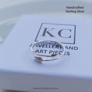 May include: A silver ring with an arrow design. The ring is handcrafted from sterling silver and is displayed on a white box with the text "KC Jewellery and Art Pieces" and "JewelleryCraftbyKC.etsy.com".