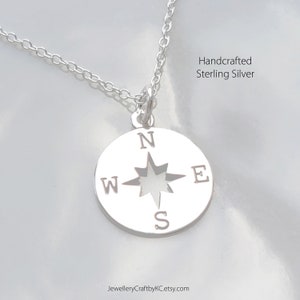 May include: A silver necklace with a compass pendant. The compass has a cut-out star in the center and the letters N, S, E, and W around the edge. The necklace is handcrafted from sterling silver.