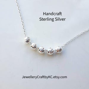 May include: A handcrafted sterling silver necklace featuring five faceted, spherical beads strung on a delicate chain. The necklace is displayed on a white surface. Text on the image reads "Handcraft Sterling Silver" and "JewelleryCraftbyKC.etsy.com".
