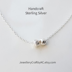 May include: A delicate sterling silver necklace featuring two textured beads. The necklace is hand-crafted and the text "Handcraft Sterling Silver" is displayed at the top. The Etsy shop name "JewelleryCraftbyKC.etsy.com" is displayed at the bottom.