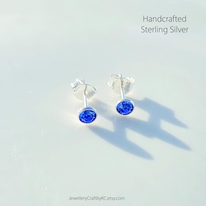 May include: A pair of handcrafted sterling silver stud earrings with small blue gemstones.