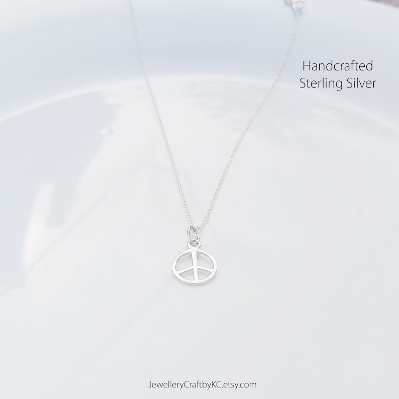 May include: A silver peace sign pendant necklace on a white background. Handcrafted Sterling Silver.