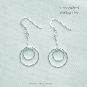 Puede incluir: Un par de pendientes de plata con dos círculos entrelazados. Los pendientes están hechos a mano en plata de ley.