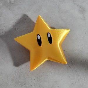 May include: A gold star-shaped figurine with black eyes. The star has a shiny, metallic finish.