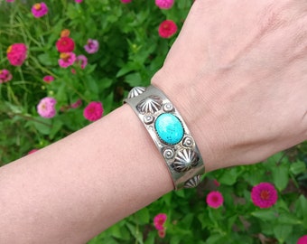 Puede incluir: Un brazalete de plata con piedras turquesa y un diseño decorativo. El brazalete se lleva en la muñeca.