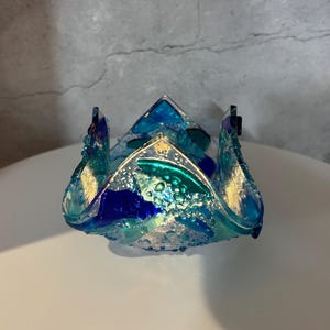 May include: A decorative glass bowl with a unique, textured design. The bowl features shades of blue, teal, and gold, with a bubbly, ocean-like appearance. The bowl is likely handmade and adds a touch of artistic flair to any space.