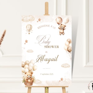 May include: A baby shower sign with a soft, neutral color palette. The sign features a teddy bear holding balloons, an air balloon, and the words "Baby Shower de Abigail" in elegant script. The date "17 septembre 2025" is also displayed.