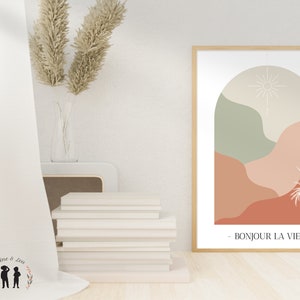 May include: A framed print with a minimalist abstract design featuring a sun, arch, and stylized plants in shades of green, beige, and orange. The text "BONJOUR LA VIE" is printed below the design.