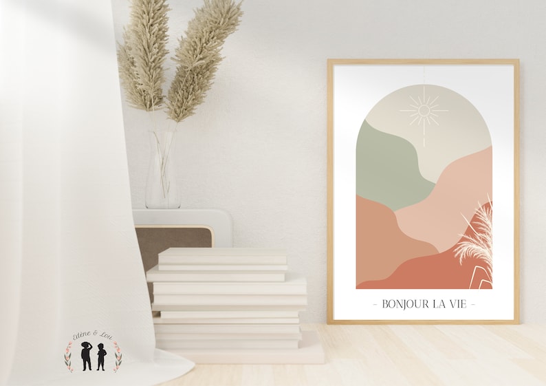 May include: A framed print with a minimalist abstract design featuring a sun, arch, and stylized plants in shades of green, beige, and orange. The text "BONJOUR LA VIE" is printed below the design.