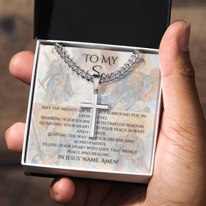 Könnte beinhalten: Eine silberfarbene Kreuz-Anhänger-Halskette in einer schwarzen Box. Die Halskette hat eine Panzerkette und einen Kreuz-Anhänger. Die Box enthält den Text "TO MY S" und weitere Texte über Glauben und Segen.