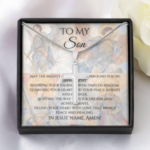 Könnte beinhalten: Eine silberne Kreuz-Anhänger-Halskette in einer schwarzen Geschenkbox. Auf der Box steht "TO MY Son" und eine religiöse Botschaft. Das Kreuz hängt an einer silbernen Kette, mit einem detaillierten Hintergrund.