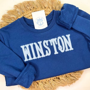 May include: A navy blue sweatshirt with the name "WINSTON" embroidered in light blue on the front.