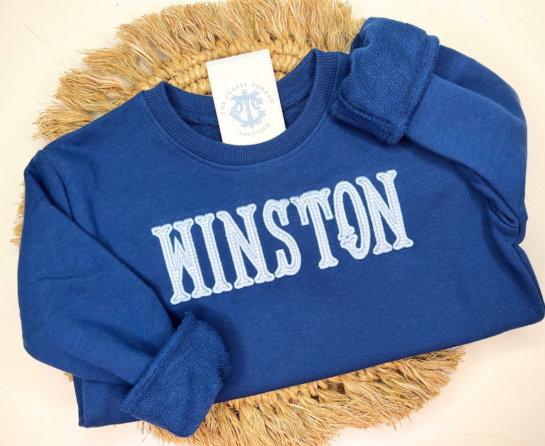 May include: A navy blue sweatshirt with the name "WINSTON" embroidered in light blue on the front.