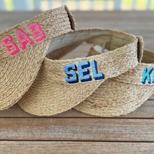 May include: Three straw visors with different colored embroidered names: "SAB" in pink, "SEL" in blue, and "KB" in turquoise.