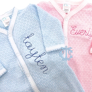 May include: Two baby onesies, one light blue with the name "Haysten" embroidered on it and one pink with the name "Everly" embroidered on it.