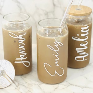 May include: Three glass can-shaped cups with lids and straws filled with iced coffee. The cups are personalized with the names "Hannah", "Emily", and "Amelia" in white lettering.