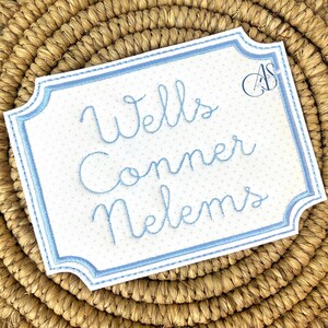 Puede incluir: Un letrero blanco bordado con un borde azul y lunares azules. El letrero dice "Wells Conner Nelms".