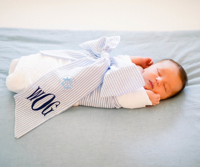 May include: A newborn baby swaddled in a blue and white striped blanket with the monogram "WOG" embroidered on it.