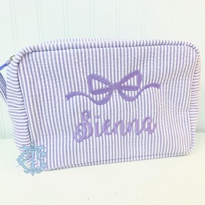 May include: A lavender and white striped makeup bag with a purple embroidered bow and the name "Sienna" on it.
