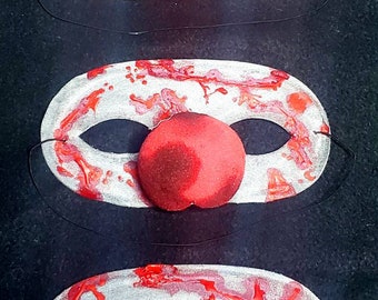 May include: Three silver masquerade masks with red paint splatters and red felt noses. The masks have black eye holes and are attached to black elastic strings.