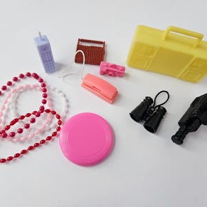 May include: A collection of miniature toys, including a yellow suitcase, a pink frisbee, a purple cell phone, a brown radio, a pink camera, a pink telephone, black binoculars, a black toy gun, and three beaded necklaces.