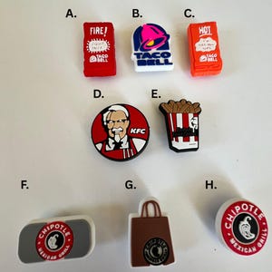 May include: A collection of colorful shoe charms featuring fast food logos. Includes Taco Bell sauce packets, a Taco Bell bell, KFC's Colonel Sanders, a container of fries, and Chipotle logos.