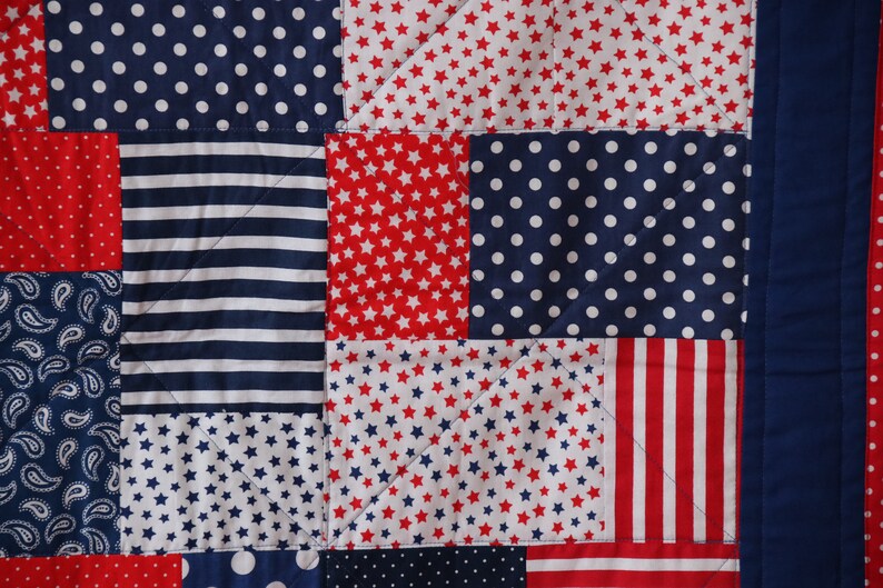 Puede incluir: Una colcha de retazos con un esquema de color rojo, blanco y azul. La colcha est&aacute; hecha de diferentes telas con varios patrones, incluyendo estrellas, rayas, lunares y paisley.